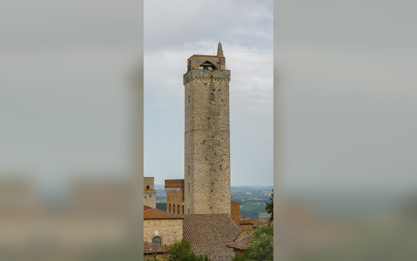 Tall stone bell tower rises above tiled rooftops in San Gimignano